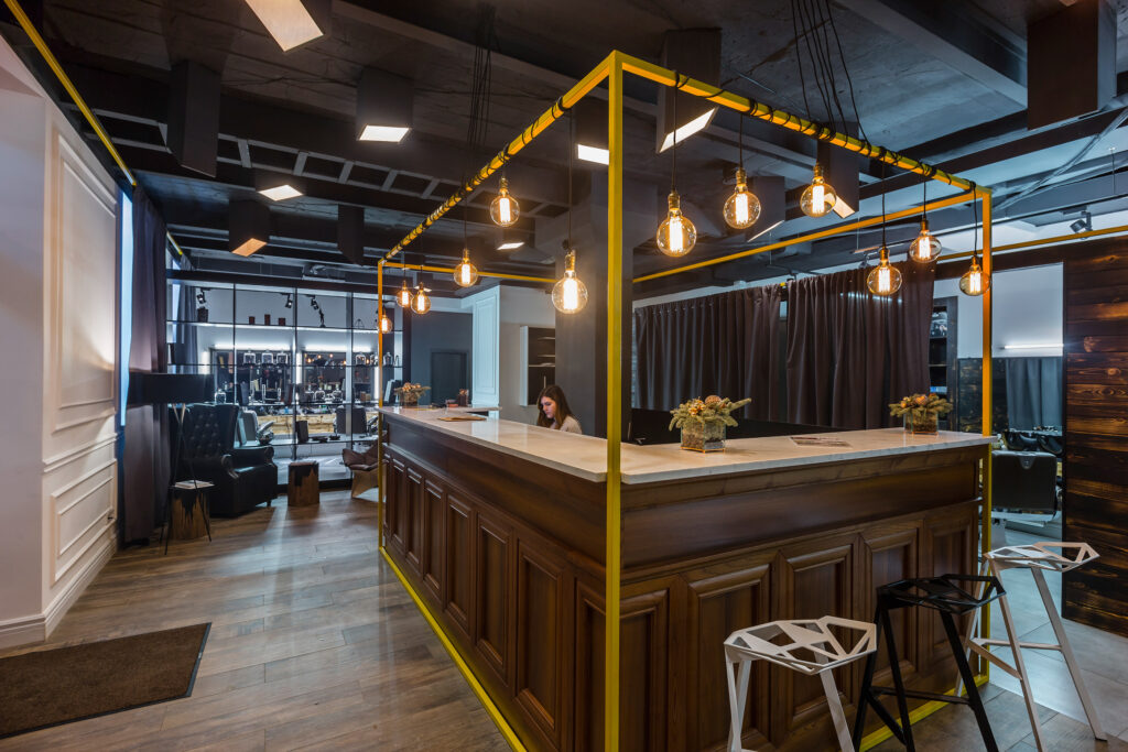 cozy barbershop with candles in fire place, geometrical chairs, & bar themed front desk. White, brown, & dark brown color scheme.