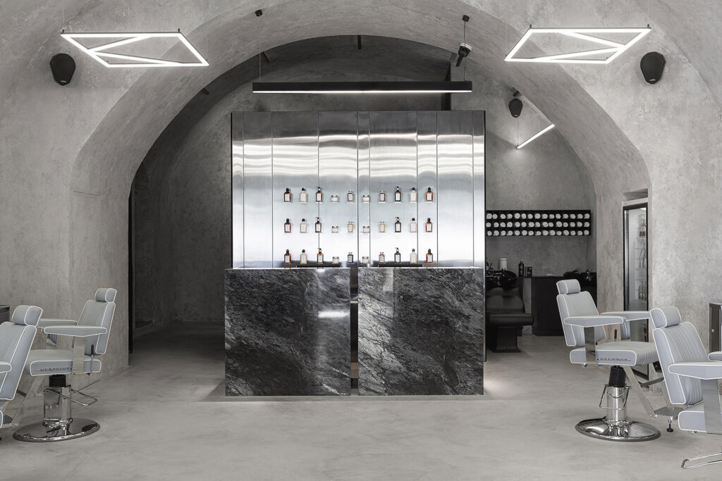 Grey & white barbershop with white & grey chairs & granite display case with product bottles in center of the room 